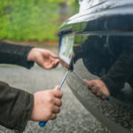 Persona che rimuove la targa di un’auto con un cacciavite durante la sostituzione della targa auto