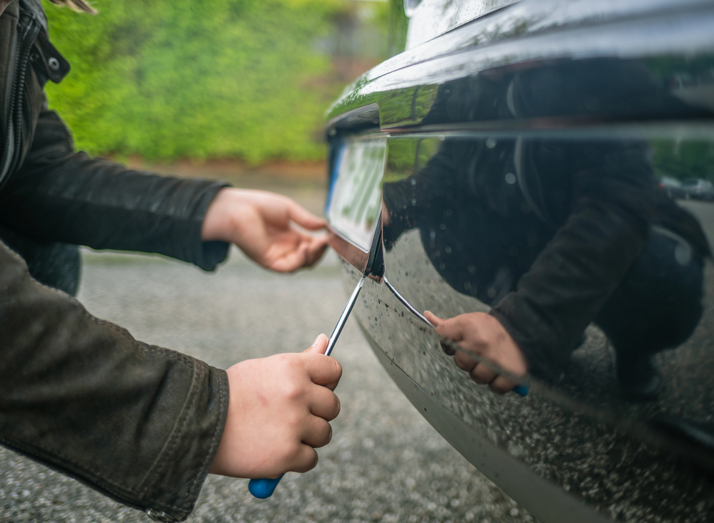 Persona che rimuove la targa di un’auto con un cacciavite durante la sostituzione della targa auto